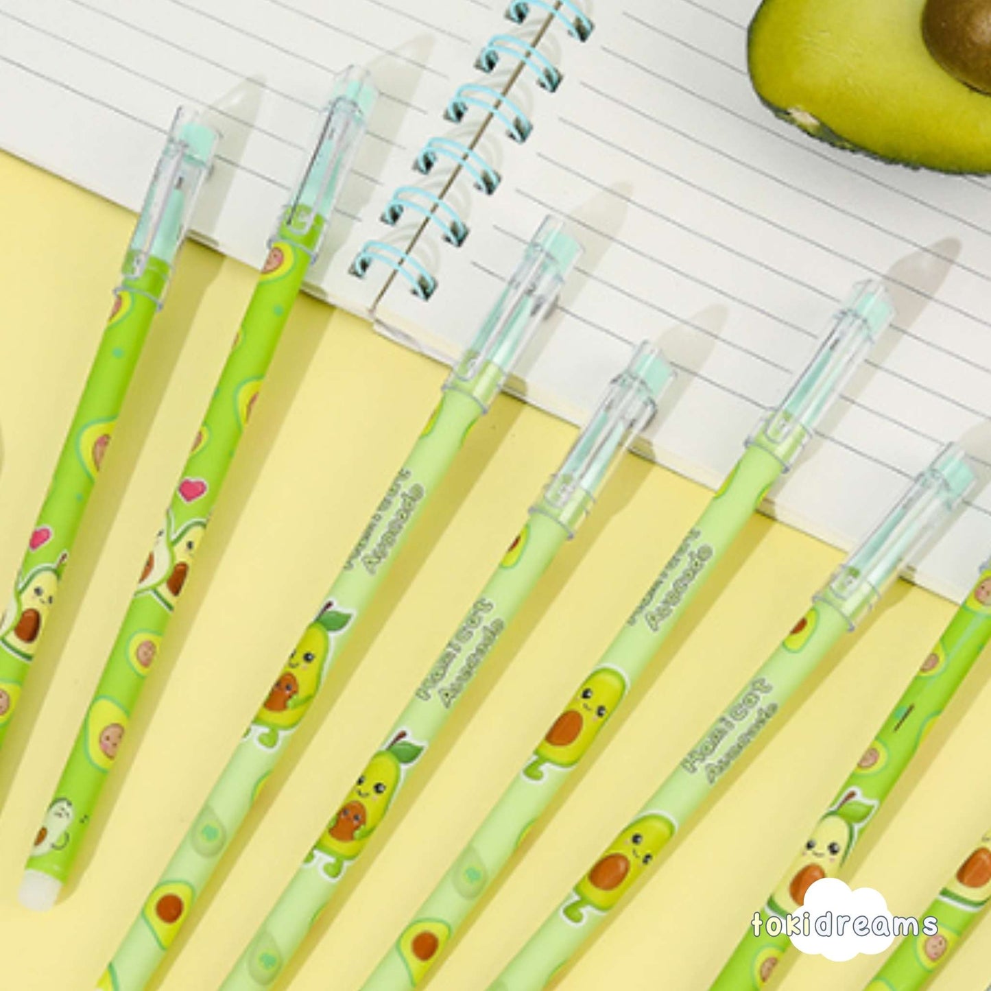 Avocado design pens on a notebook with a cut avocado and green background