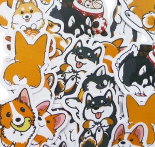 A pile of die-cut stickers featuring cute cartoon dog illustrations, including Shiba Inu, Corgi, and Husky dogs in orange, black, white, and red.