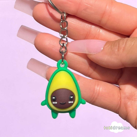 Hand holding mini keychain shaped like an avocado with a happy face in green and yellow color.