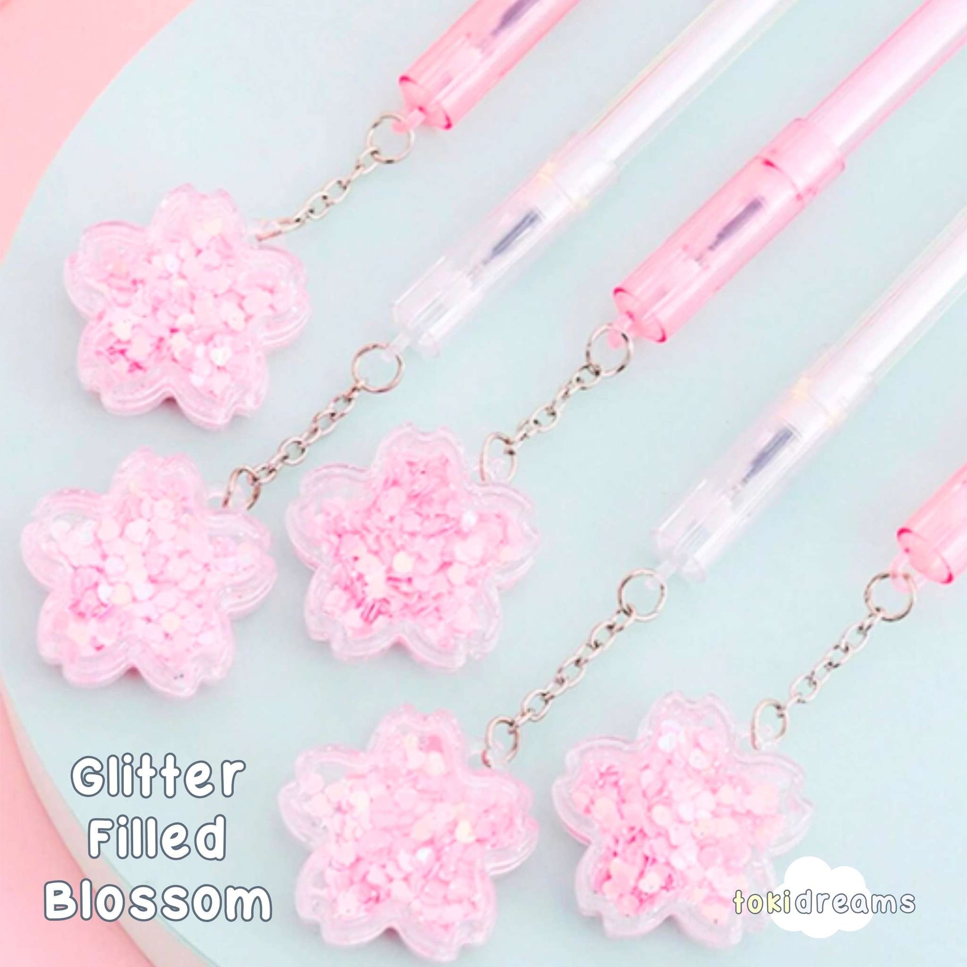 A collection of Sakura Blossom Gel Pens with pink flower designs and transparent handles, displayed on a surface with a pink background.